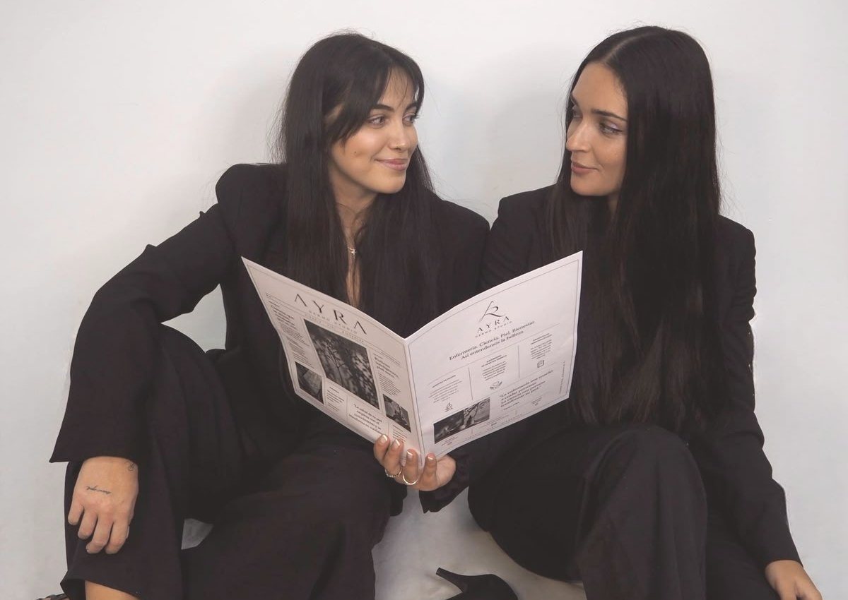 Alba y Raquel, fundadoras de AYRA, leyendo juntas el periódico AYRA Dermo Studio
